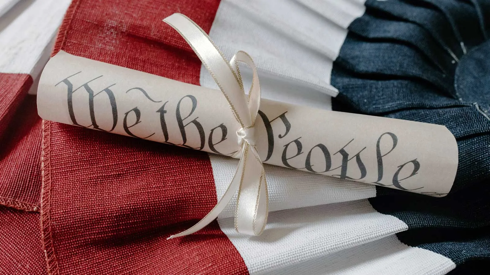 Photo of rolled up paper labeled "We the people" on bunting of red, white and blue